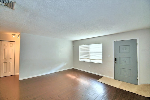 interior space with a textured ceiling, dark wood-style flooring, visible vents, and baseboards