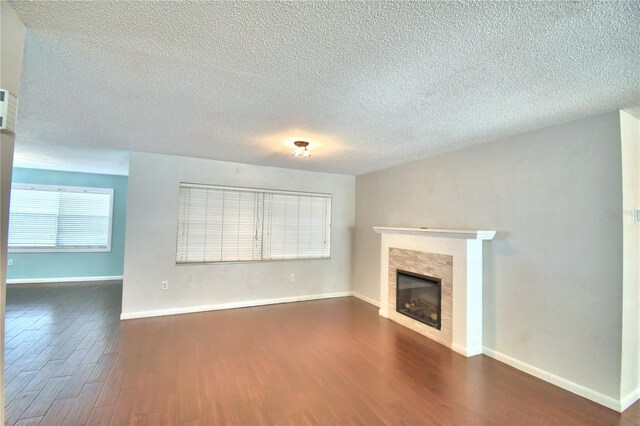 unfurnished living room featuring a tiled fireplace, a textured ceiling, and dark wood-type flooring