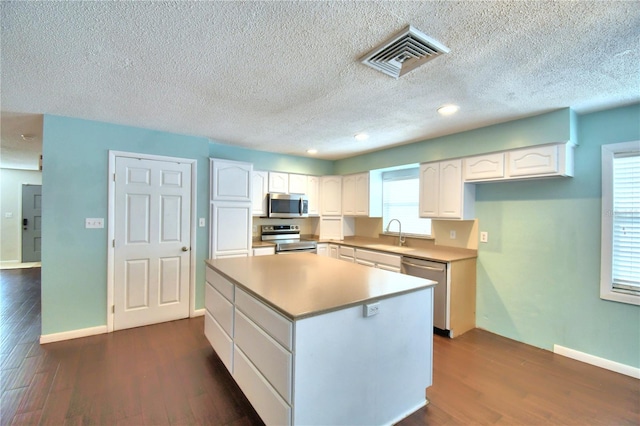 kitchen with stainless steel appliances, a textured ceiling, dark hardwood / wood-style floors, white cabinets, and a kitchen island