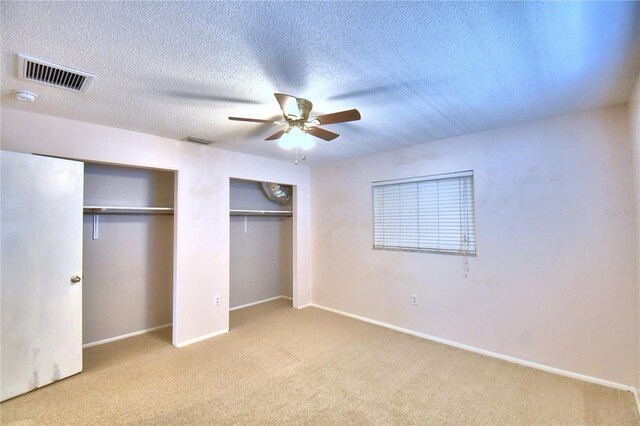 unfurnished bedroom with ceiling fan, multiple closets, a textured ceiling, and light carpet