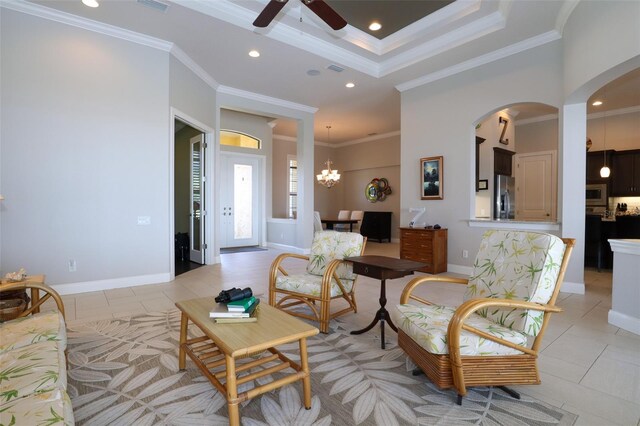 tiled living room with a tray ceiling, ceiling fan with notable chandelier, and ornamental molding