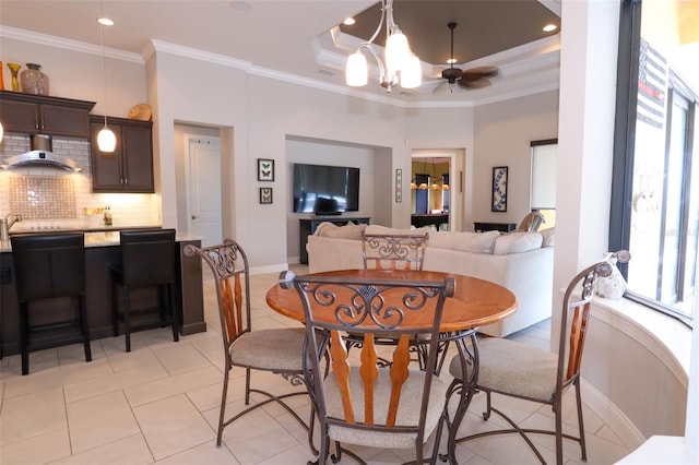 dining space featuring ornamental molding, light tile patterned floors, ceiling fan with notable chandelier, and a tray ceiling