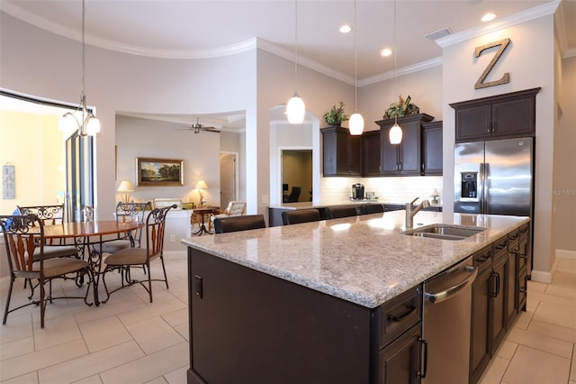 kitchen featuring decorative light fixtures, decorative backsplash, appliances with stainless steel finishes, a kitchen island with sink, and a sink