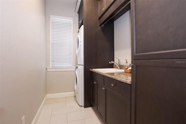 clothes washing area with light tile patterned floors, a sink, stacked washer and clothes dryer, and baseboards