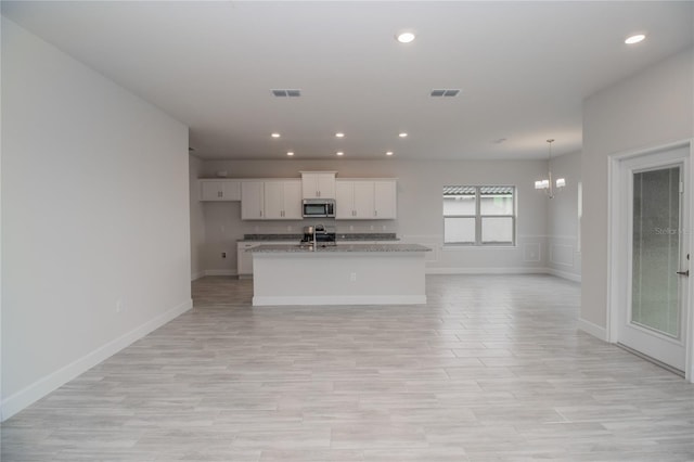 kitchen featuring white cabinetry, a chandelier, a kitchen island with sink, stone counters, and stove