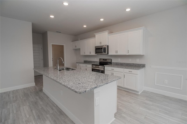 kitchen featuring white cabinetry, stainless steel appliances, light stone countertops, sink, and a center island with sink