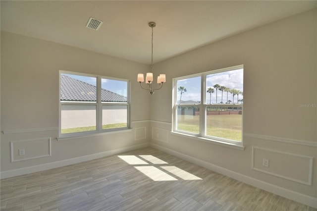 unfurnished room with a decorative wall, light wood finished floors, a chandelier, and visible vents