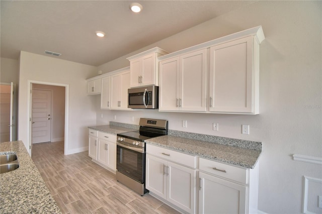 kitchen with white cabinetry, light stone countertops, stainless steel appliances, wood finish floors, and visible vents