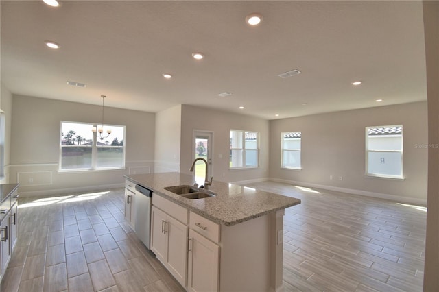 kitchen featuring a center island with sink, white cabinetry, a sink, open floor plan, and stainless steel dishwasher