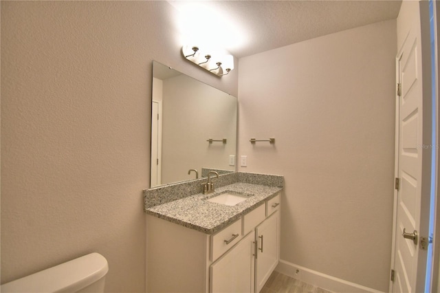 half bathroom with baseboards, toilet, and vanity