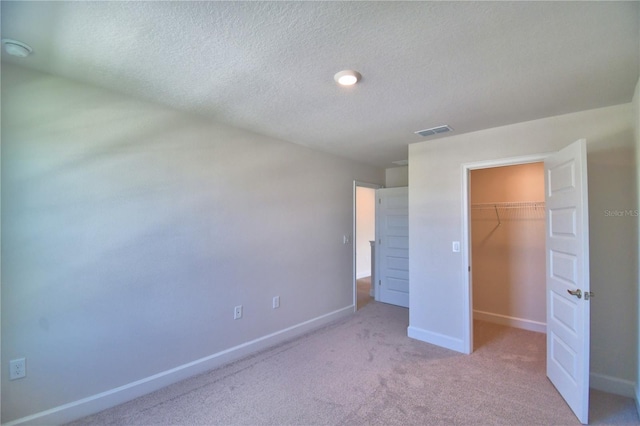 unfurnished bedroom featuring a walk in closet, baseboards, carpet floors, visible vents, and a closet