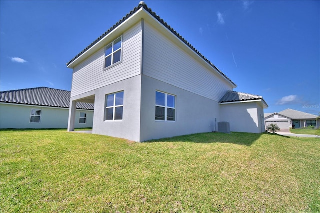 back of property featuring a lawn, a tile roof, central air condition unit, and stucco siding