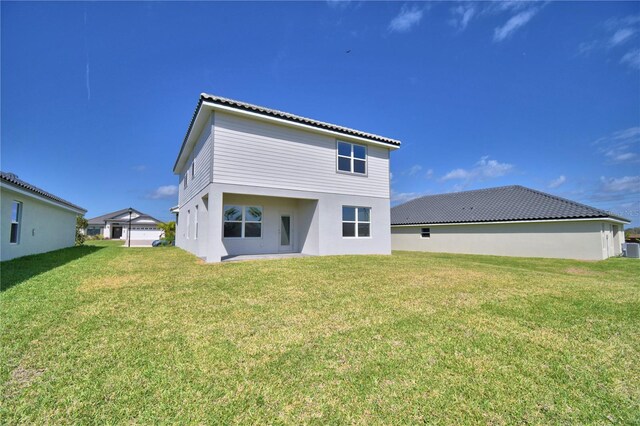 rear view of house with stucco siding, central AC, and a yard