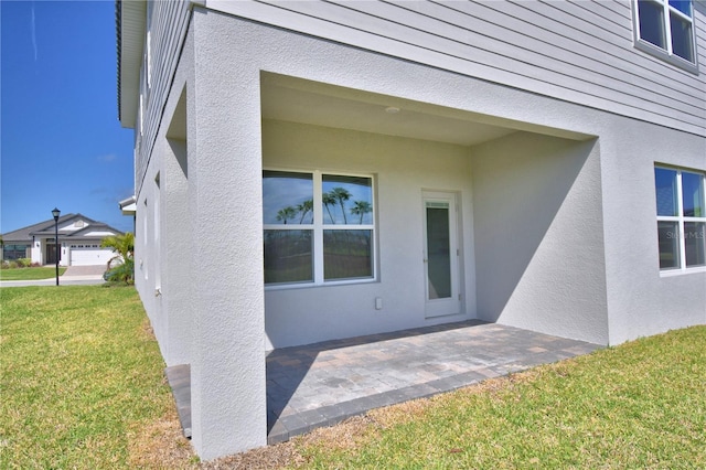 entrance to property with stucco siding, a patio area, and a yard
