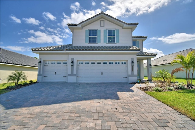 mediterranean / spanish-style house with stucco siding, a tile roof, a garage, and decorative driveway