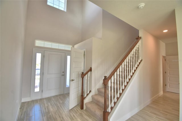 foyer featuring stairway, a towering ceiling, baseboards, and light wood finished floors