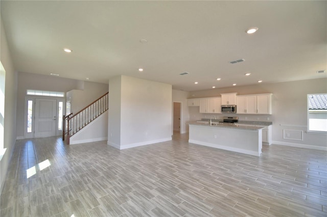 kitchen with open floor plan, stainless steel microwave, white cabinetry, and visible vents