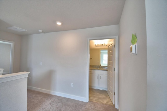 corridor with light colored carpet, recessed lighting, baseboards, and a sink