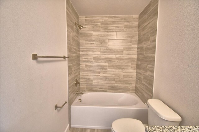 bathroom with a textured wall, toilet, and shower / tub combination