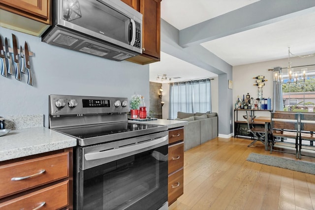 kitchen with appliances with stainless steel finishes, hanging light fixtures, brown cabinets, a notable chandelier, and light wood finished floors