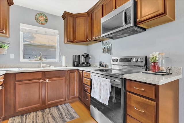 kitchen featuring a sink, light wood-type flooring, appliances with stainless steel finishes, and brown cabinetry