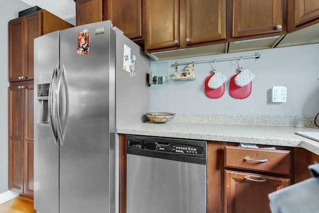 kitchen with stainless steel appliances, brown cabinets, and light stone counters