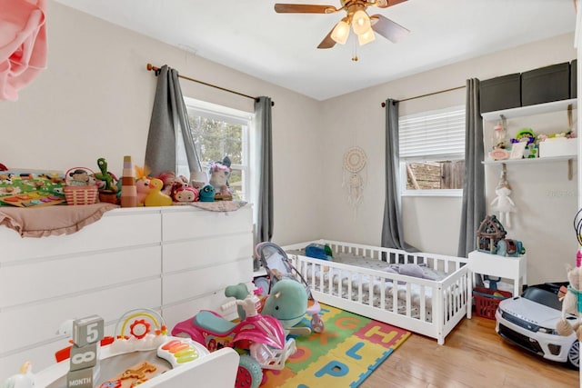 bedroom featuring ceiling fan, a crib, and light wood-style floors