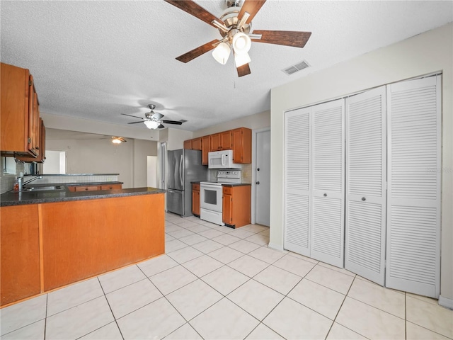 kitchen with visible vents, a sink, dark countertops, white appliances, and a peninsula