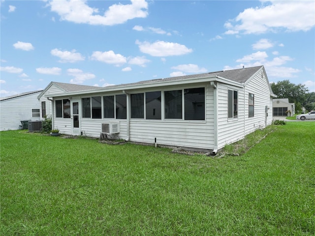 view of front of home with an AC wall unit, central AC unit, a front yard, and a sunroom