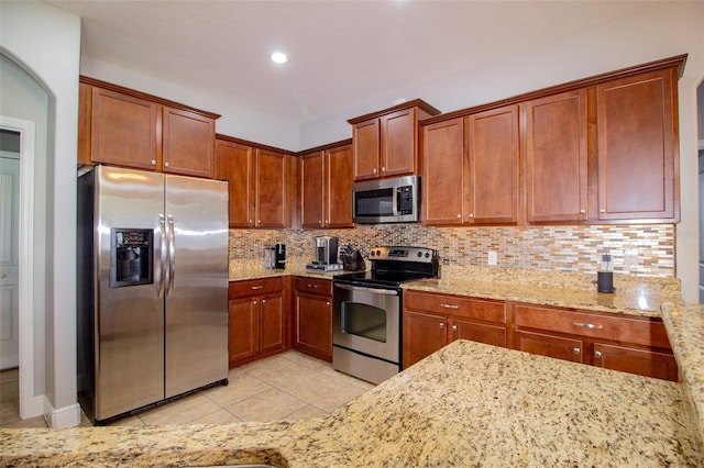 kitchen featuring light tile patterned floors, decorative backsplash, appliances with stainless steel finishes, brown cabinetry, and light stone countertops