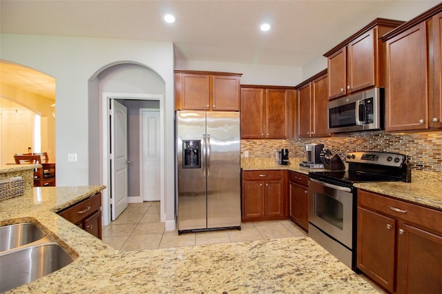 kitchen with light tile patterned floors, light stone counters, a sink, appliances with stainless steel finishes, and backsplash