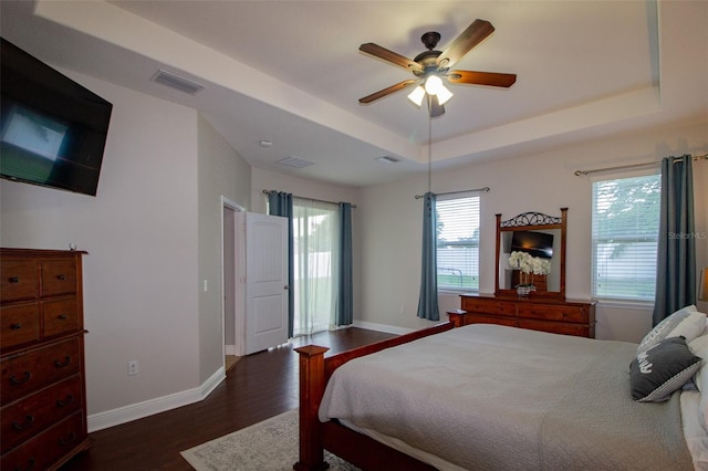 bedroom featuring a ceiling fan, visible vents, baseboards, dark wood-style floors, and a raised ceiling