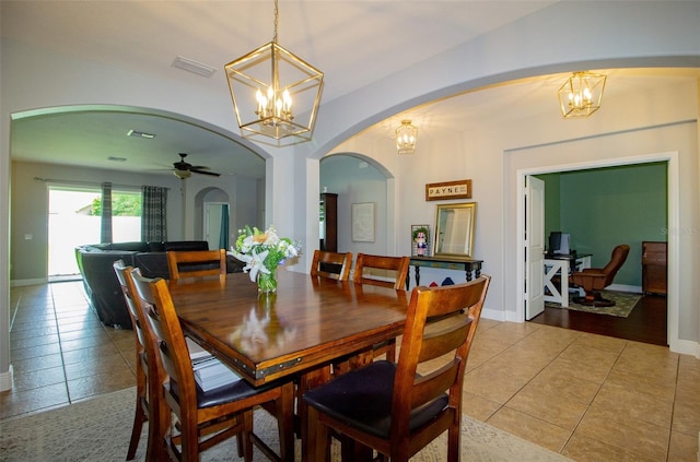 tiled dining room with arched walkways, visible vents, baseboards, and ceiling fan with notable chandelier