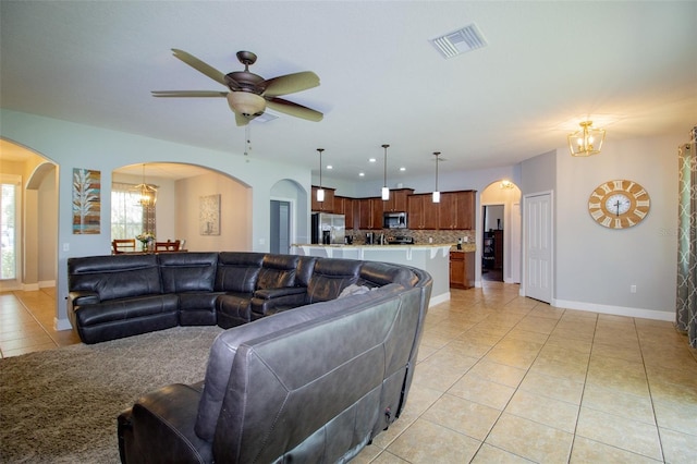 living area featuring baseboards, visible vents, arched walkways, light tile patterned flooring, and ceiling fan with notable chandelier