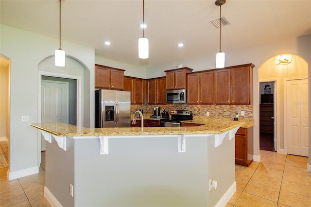 kitchen with arched walkways, a breakfast bar area, stainless steel appliances, decorative backsplash, and light tile patterned flooring