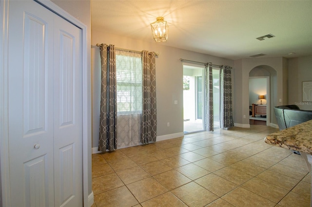 interior space featuring arched walkways, a notable chandelier, visible vents, light tile patterned flooring, and baseboards