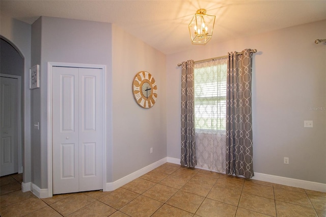 empty room featuring arched walkways, light tile patterned flooring, baseboards, and an inviting chandelier