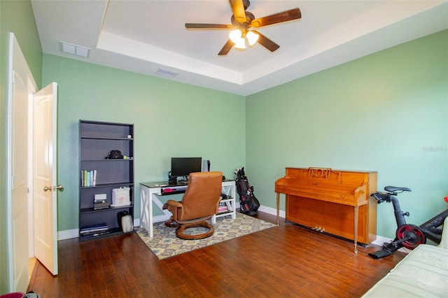 office featuring a tray ceiling, visible vents, baseboards, and wood finished floors