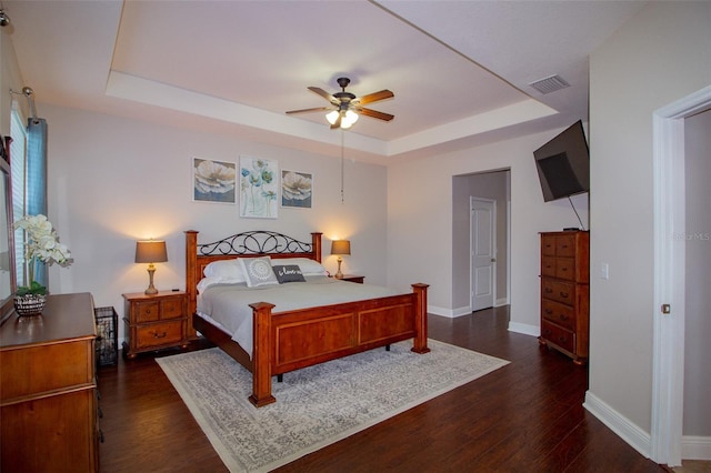 bedroom with dark wood-style floors, a raised ceiling, visible vents, and baseboards