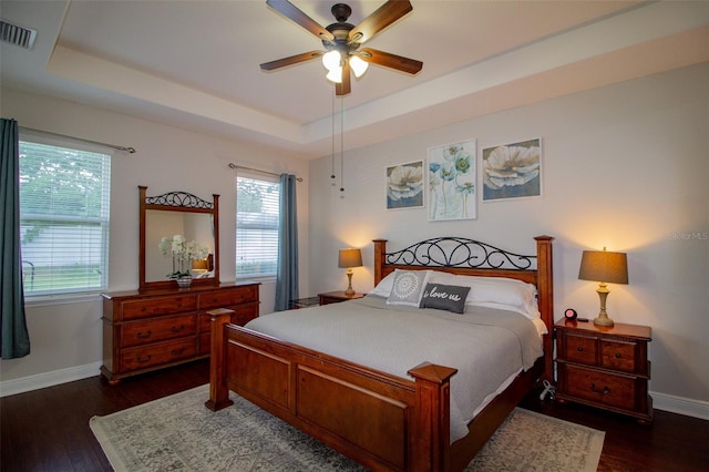 bedroom with dark wood-style floors, a raised ceiling, visible vents, and baseboards