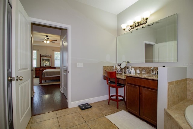 bathroom with connected bathroom, vanity, baseboards, tile patterned floors, and tiled tub