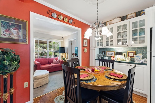 dining area with dark wood-type flooring, an inviting chandelier, and ornamental molding