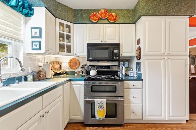 kitchen featuring light wood-type flooring, stainless steel range with gas stovetop, tasteful backsplash, sink, and white cabinets