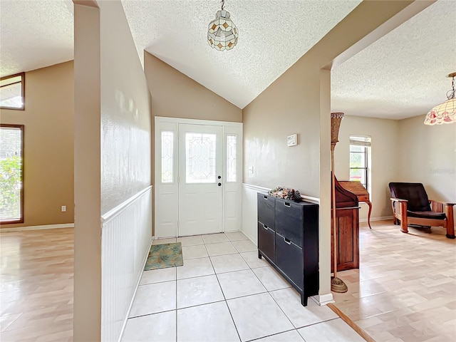 foyer featuring light tile patterned flooring, a textured ceiling, and vaulted ceiling