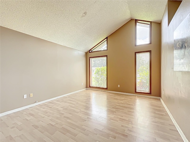 empty room with light wood-type flooring, high vaulted ceiling, baseboards, and a textured ceiling