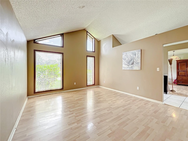 empty room featuring a textured ceiling, high vaulted ceiling, baseboards, and light wood-style floors