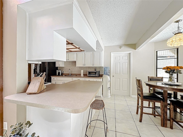 kitchen with white cabinets, a kitchen breakfast bar, a peninsula, light countertops, and light tile patterned flooring