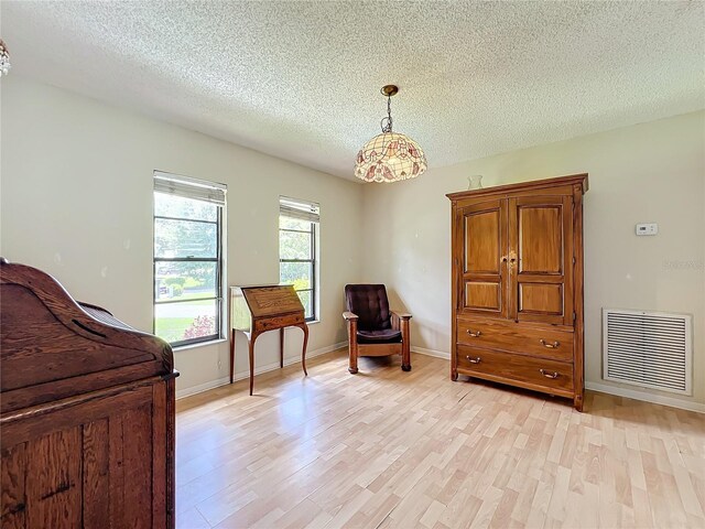 bedroom featuring light wood-type flooring, baseboards, visible vents, and a textured ceiling