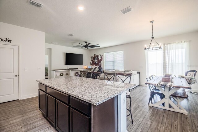 kitchen with ceiling fan with notable chandelier, dark brown cabinets, hanging light fixtures, a center island, and light wood-type flooring