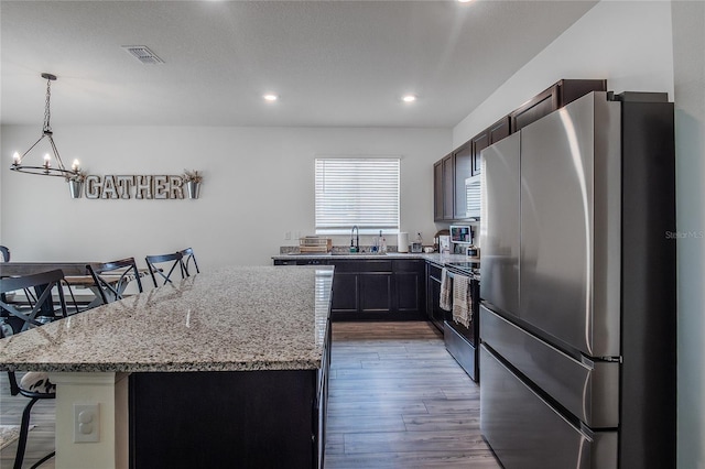 kitchen featuring stainless steel refrigerator, a center island, wood-type flooring, range with electric stovetop, and a kitchen bar